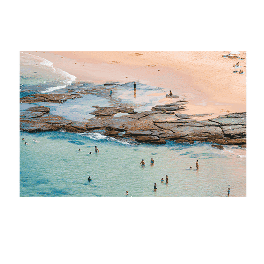 A close-up aerial view of Bateau Bay, NSW, capturing swimmers enjoying the shallow, crystal-clear waters near the rocky shoreline. The warm golden sand contrasts with the turquoise sea, creating a vibrant coastal scene.
