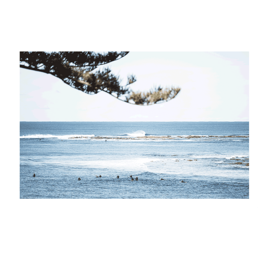 Aerial view of surfers floating in the deep blue waters of Blue Bay, NSW, surrounded by rolling waves. ​​