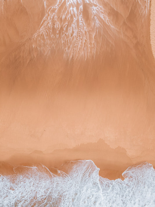 Aerial view of Copacabana Beach, NSW, showcasing intricate sand patterns and foamy waves meeting the golden shoreline.
