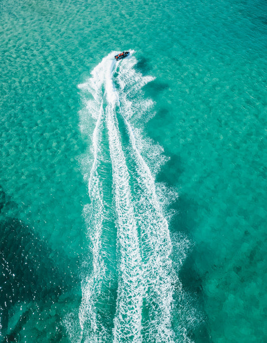 A breathtaking aerial view of a speedboat cutting through the clear aqua waters of Frazer Beach, NSW, leaving a dynamic white trail in its wake.