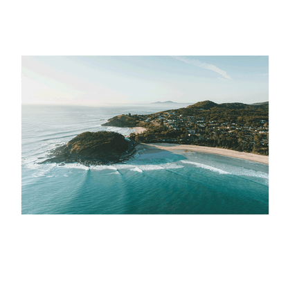 A breathtaking aerial view of Scotts Head, NSW, bathed in golden morning light. Waves roll onto the pristine beach as the coastal town nestles between lush green hills, creating a serene and picturesque seascape.
