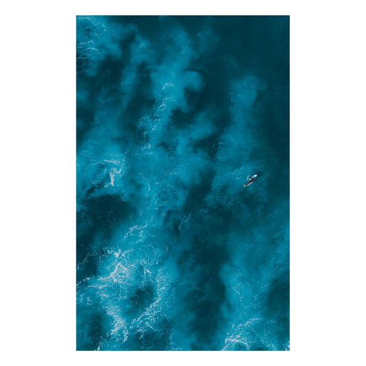 Experience the power of Angourie Beach with Brave – an aerial ocean print capturing a lone surfer paddling into vast, deep blue waters. A moody and dramatic seascape.