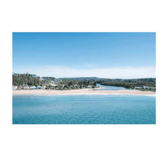 Aerial view of Avoca Beach, NSW, where the golden sandbar separates the tranquil lagoon from the rolling ocean waves, bathed in soft morning light.