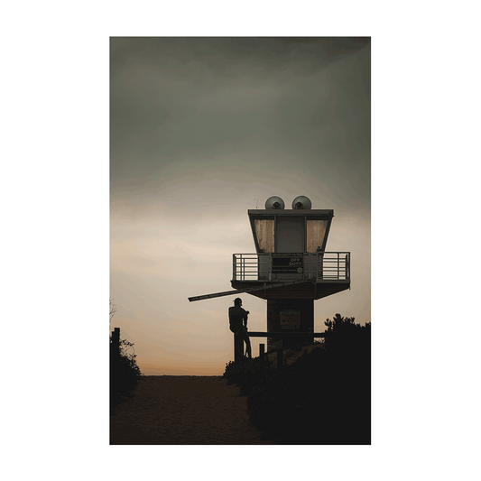 A moody coastal scene at Avoca Beach, NSW, featuring a silhouetted figure near a lifeguard tower under a dramatic sky at dusk.