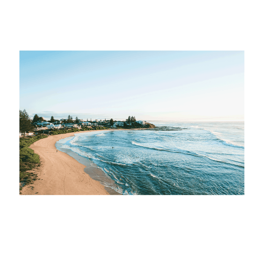 A scenic morning view of Blue Bay, NSW, featuring rolling waves, golden sand, and coastal homes under soft winter light.