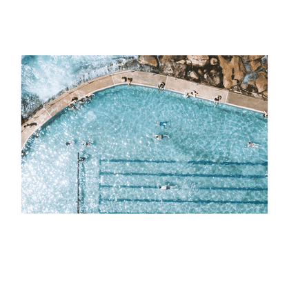 A sunlit aerial view of Bronte’s ocean pool in Sydney, featuring swimmers enjoying crystal-clear turquoise water with waves gently lapping at the pool’s edge.