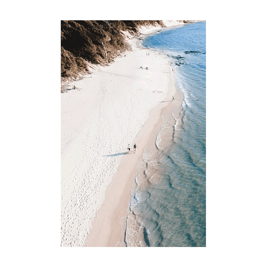 A stunning aerial beach print of Clarkes Beach, Byron Bay, NSW, showcasing soft white sand, gentle waves, and beachgoers strolling along the coastline.