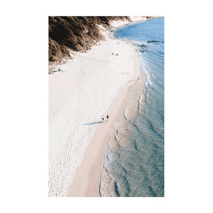 A stunning aerial beach print of Clarkes Beach, Byron Bay, NSW, showcasing soft white sand, gentle waves, and beachgoers strolling along the coastline.