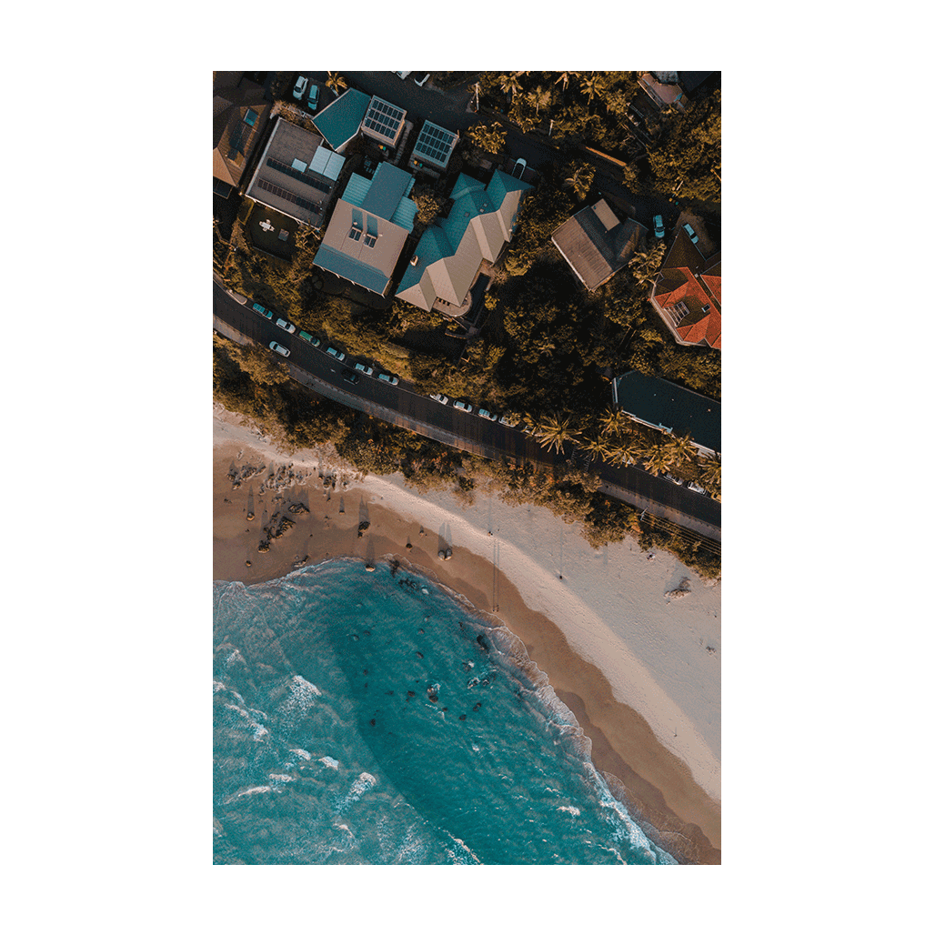 A stunning aerial print of Byron Bay, NSW, showcasing colourful beach houses, palm trees, and golden sandy shores at sunset. A perfect coastal scene.