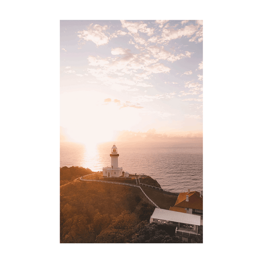 A breathtaking aerial print of Byron Bay Lighthouse at sunrise, capturing soft golden light, rolling clouds, and ocean views from Australia's most easterly point.