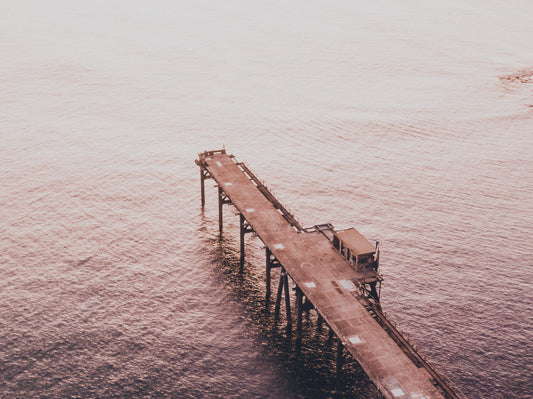 Aerial view of Catherine Hill Bay’s jetty bathed in soft, golden light, with calm waters reflecting the warm hues of the sunset.
