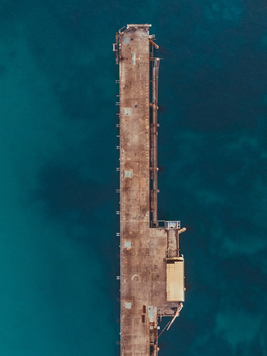 Aerial view of Catherine Hill Bay, NSW, showcasing the weathered jetty in sharp contrast to the deep turquoise ocean below.
