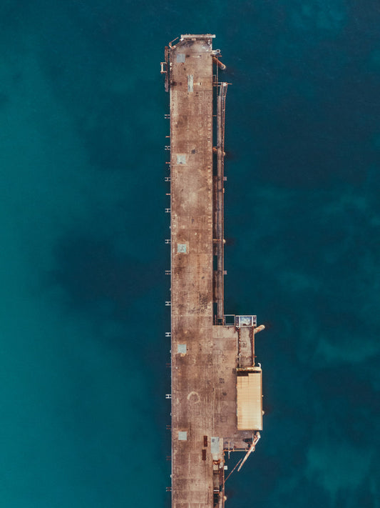 Aerial view of Catherine Hill Bay, NSW, showcasing the weathered jetty in sharp contrast to the deep turquoise ocean below.
