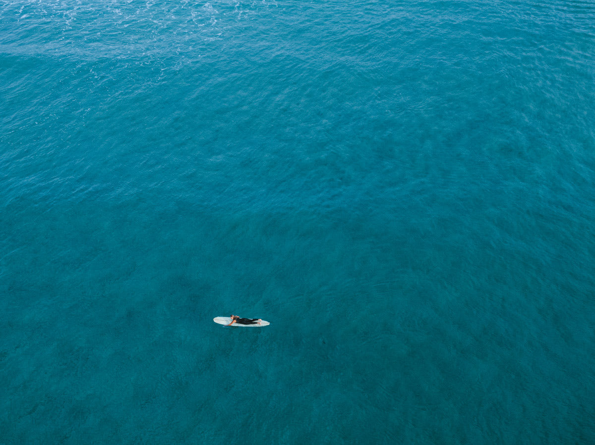 Aerial view of Catherine Hill Bay, NSW, featuring a lone surfer paddling across vibrant turquoise waters, surrounded by the calm expanse of the sea.
