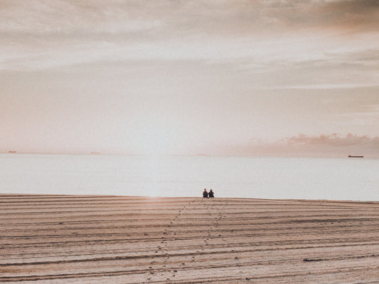 Aerial view of Catherine Hill Bay, NSW, featuring two people sitting on raked sand, gazing at the calm sunrise over serene waters.
