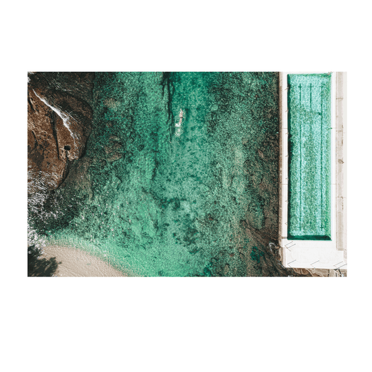 A breathtaking aerial view of Clovelly Beach, Sydney, featuring a swimmer in turquoise waters beside the structured elegance of the ocean pool.