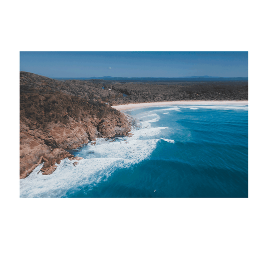 An aerial coastal print of Big Hill Beach, Crescent Head, NSW, featuring rugged cliffs, golden sand, and deep blue ocean waves crashing along the shoreline.
