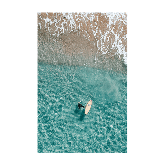 Aerial view of a surfer floating in the clear turquoise waters near the shoreline at Forresters Beach, NSW.
