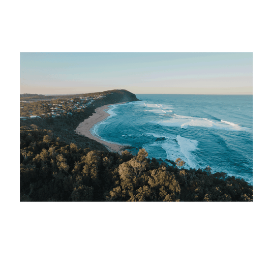 Alt Text: A breathtaking aerial view of Forresters Beach, NSW, featuring a rugged headland, rolling waves, and golden sand under a soft morning light.
