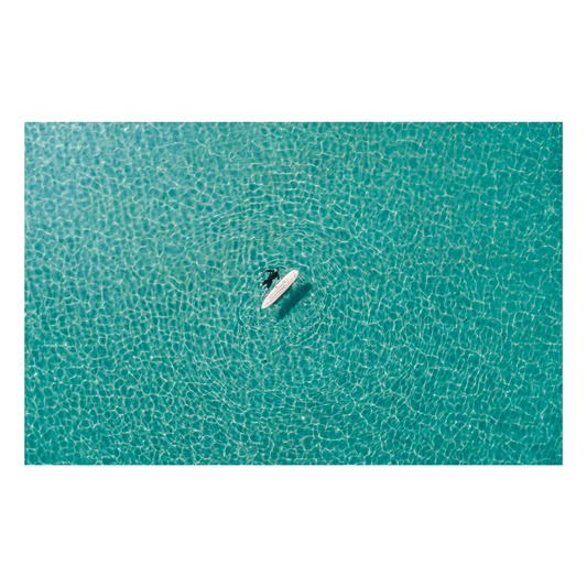 A breathtaking aerial view of a lone surfer floating in the crystal-clear waters of Forresters Beach, NSW, surrounded by sunlit ripples.