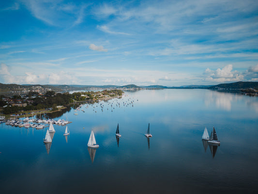 A peaceful morning scene of Gosford, NSW, featuring sailboats floating on still, reflective waters under a soft blue sky.
