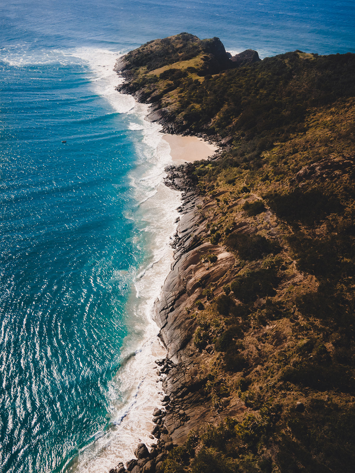 A stunning aerial view of Little Beach at Hat Head, NSW, featuring rugged cliffs, golden sands, and deep blue ocean waters.