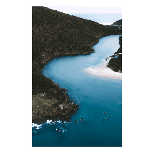 A breathtaking aerial view of Hat Head, NSW, where a winding river meets the ocean, surrounded by lush green hills.