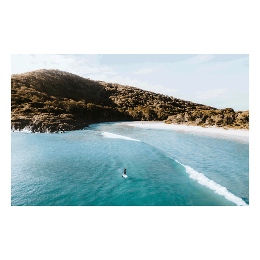 A stunning aerial view of Hat Head, NSW, featuring a lone surfer riding a wave against a backdrop of lush hills and pristine waters.