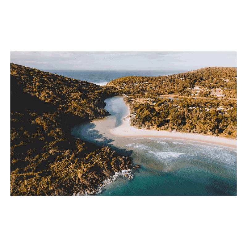 A stunning aerial view of Hat Head, NSW, showcasing a winding river meeting the ocean, surrounded by lush hills and golden sands.