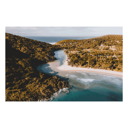 A stunning aerial view of Hat Head, NSW, showcasing a winding river meeting the ocean, surrounded by lush hills and golden sands.