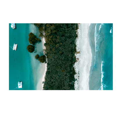 Aerial view of Huskisson on the South Coast of NSW, showcasing a striking contrast between lush greenery, pristine white sand, and vibrant turquoise waters with anchored boats nearby.