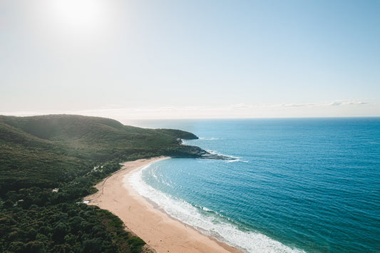 A stunning coastal view of Killcare Beach, NSW, with golden sands meeting the deep blue ocean under soft morning light.
