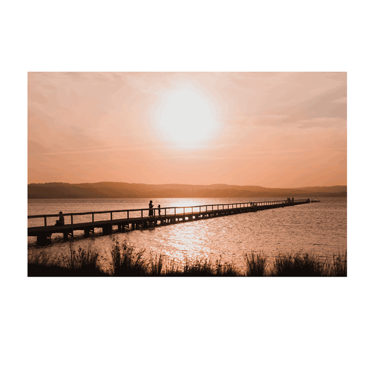 A stunning sunset at Long Jetty, NSW, with silhouettes walking along the boardwalk as golden light reflects on the water.