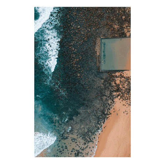 A dramatic aerial view of the ocean pool at Macmasters Beach, NSW, contrasting against the rocky shoreline and deep blue waves.