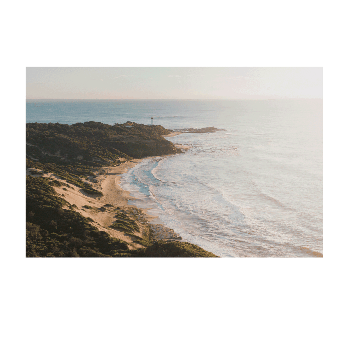 A soft, misty aerial view of Norah Head, NSW, featuring rolling sand dunes, a rugged coastline, and gentle ocean waves bathed in morning light.