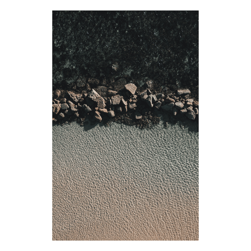 Aerial view of Soldiers Beach, NSW, highlighting the contrast between rugged coastal rocks and clear, rippled shoreline waters.