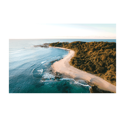 An aerial view of Soldiers Beach, Norah Head, NSW, with golden sands winding along the shoreline, turquoise waves, and the lighthouse standing in the background.