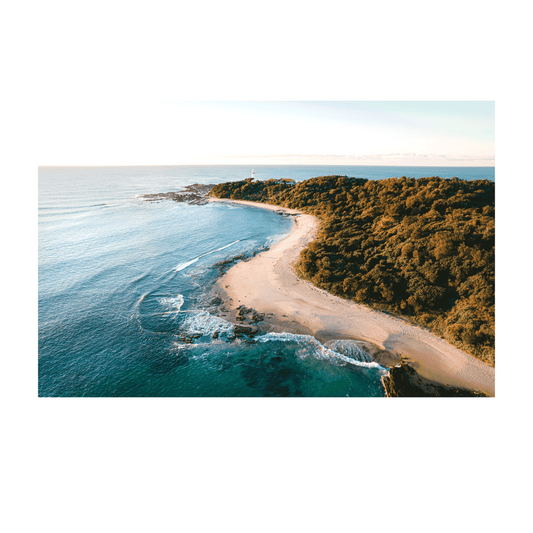 An aerial view of Soldiers Beach, Norah Head, NSW, with golden sands winding along the shoreline, turquoise waves, and the lighthouse standing in the background.