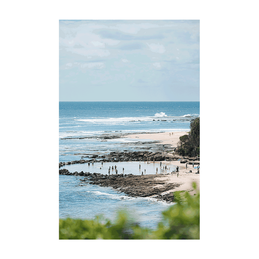 A scenic coastal view of Norah Head Beach, NSW, featuring natural rock pools filled with beachgoers, with waves rolling in the distance.