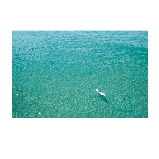 A peaceful aerial view of Norah Head Beach, NSW, featuring a lone surfer floating on crystal-clear turquoise waters.
