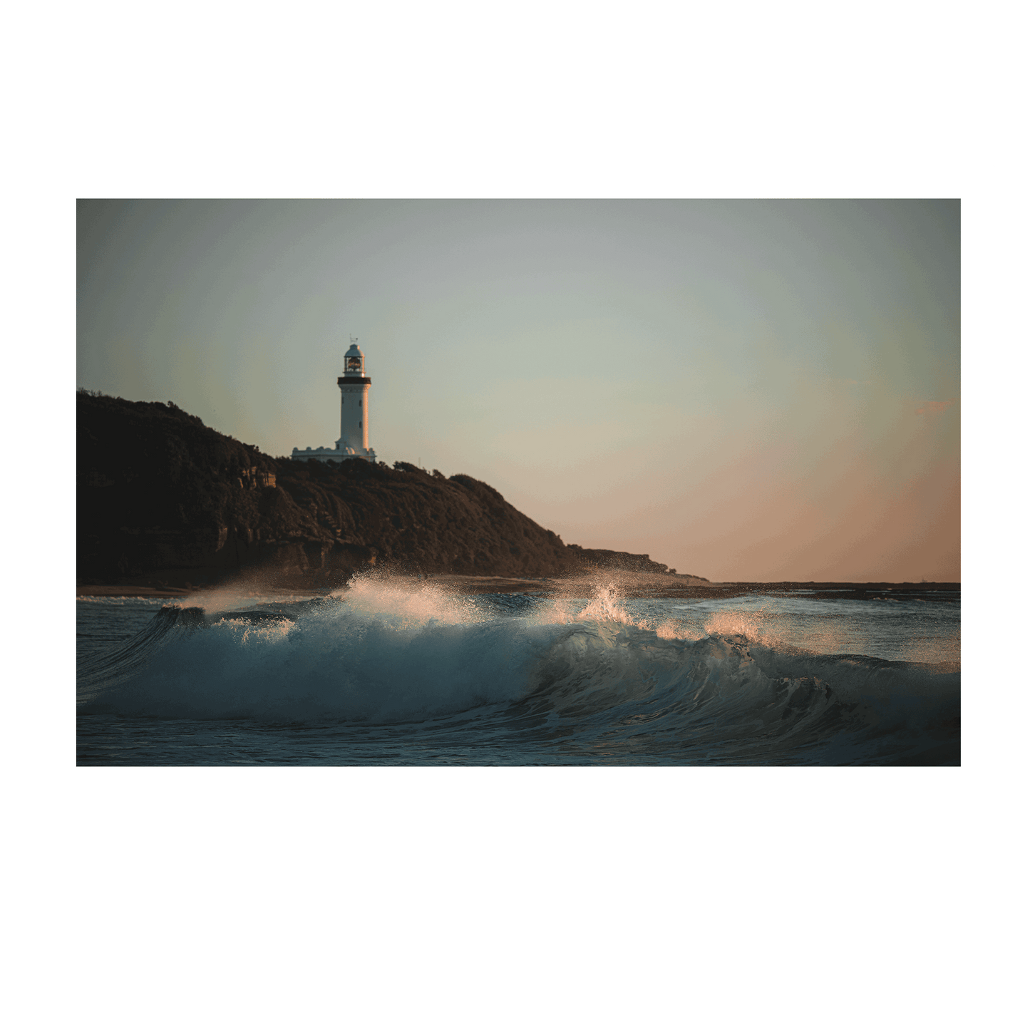 A dramatic coastal scene of Norah Head, NSW, featuring powerful waves crashing beneath the lighthouse at sunset.