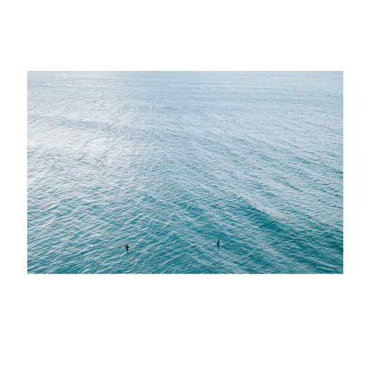 A peaceful aerial view of Norah Head, NSW, featuring two surfers floating in the vast, rippling blue ocean.
