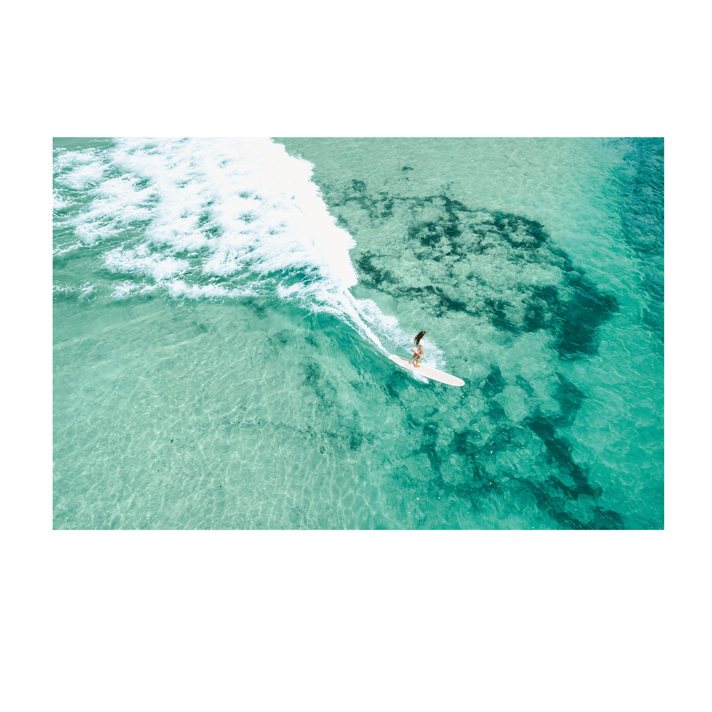 A stunning aerial view of Soldiers Beach, Norah Head, NSW, featuring a longboard surfer riding a wave over a vibrant reef.