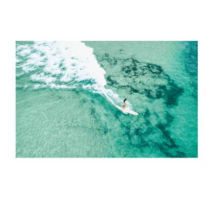 A stunning aerial view of Soldiers Beach, Norah Head, NSW, featuring a longboard surfer riding a wave over a vibrant reef.