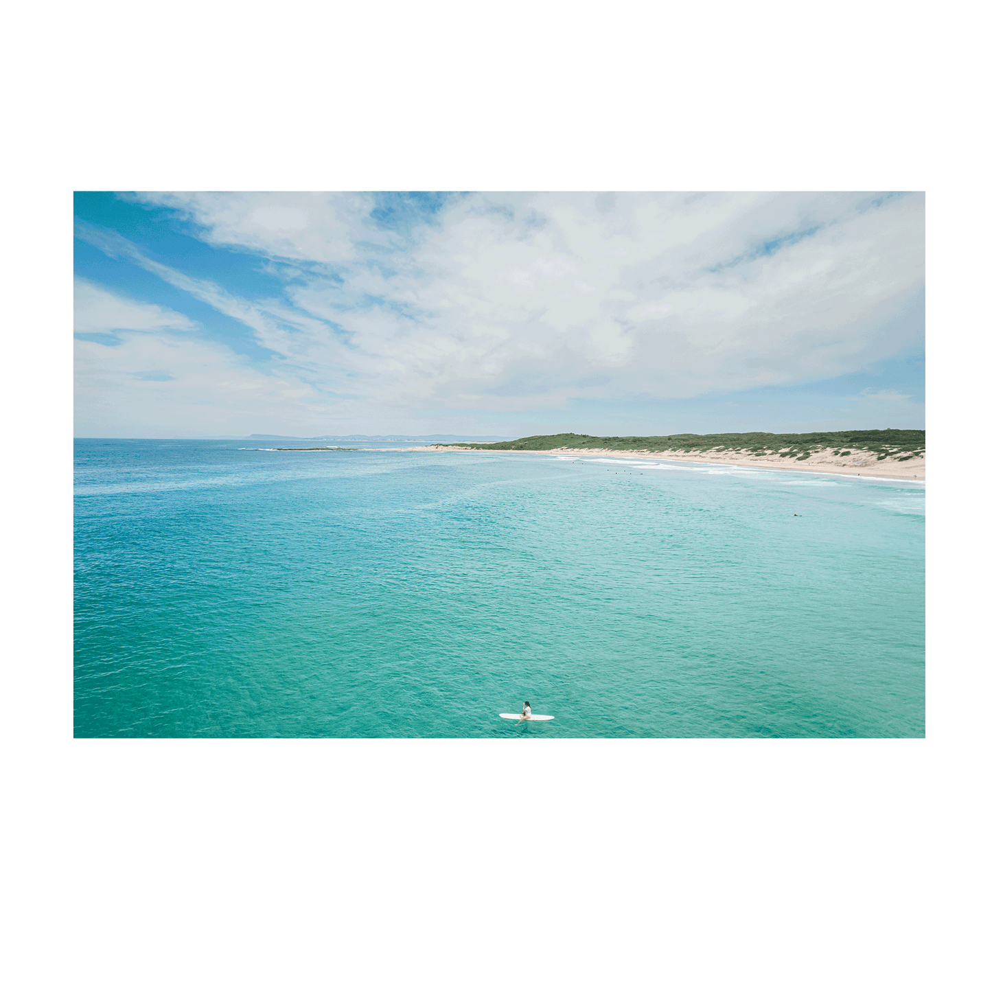 A breathtaking coastal aerial view of Soldiers Beach, Norah Head, NSW, featuring a lone surfer in turquoise waters with rolling dunes in the background.
