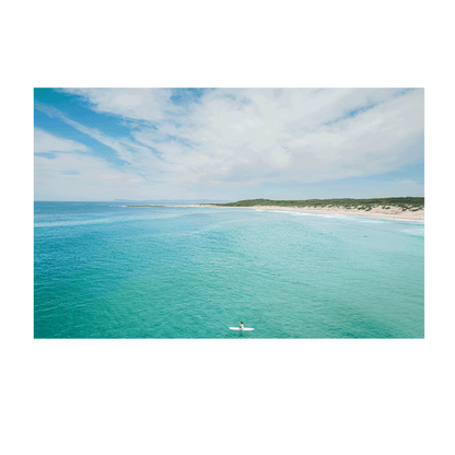 A breathtaking coastal aerial view of Soldiers Beach, Norah Head, NSW, featuring a lone surfer in turquoise waters with rolling dunes in the background.
