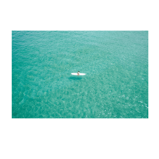 A serene aerial view of Soldiers Beach, Norah Head, NSW, featuring a lone surfer floating on tranquil, crystal-clear aqua waters.