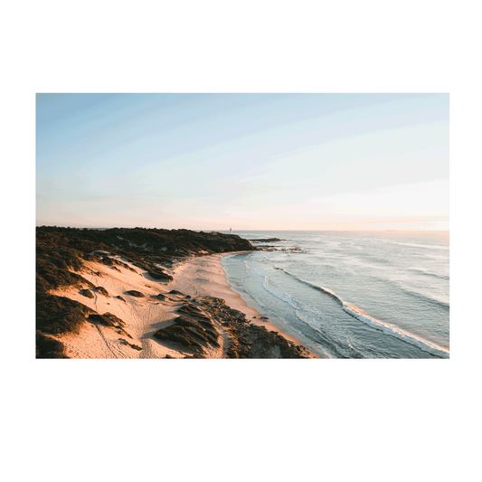 A stunning aerial view of Norah Head, NSW, featuring golden sand dunes and soft ocean waves illuminated by morning light.
