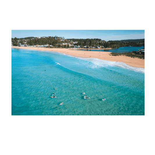 Aerial view of North Avoca Beach, NSW, with surfers floating in the turquoise waters, featuring a striking pink surfboard adding a vibrant pop of colour.