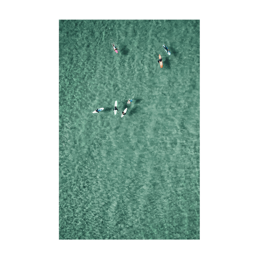 Aerial view of surfers and paddleboarders floating together in the clear turquoise waters of North Avoca Beach, NSW, enjoying a peaceful ocean moment.